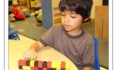 Boy sitting at table playing with small, multicolored blocks